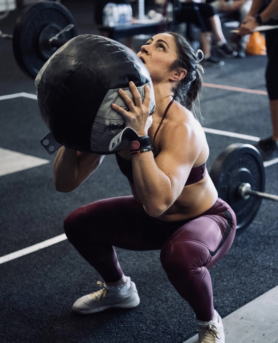Emelye mid-lift with a sandbag during a CrossFit competition