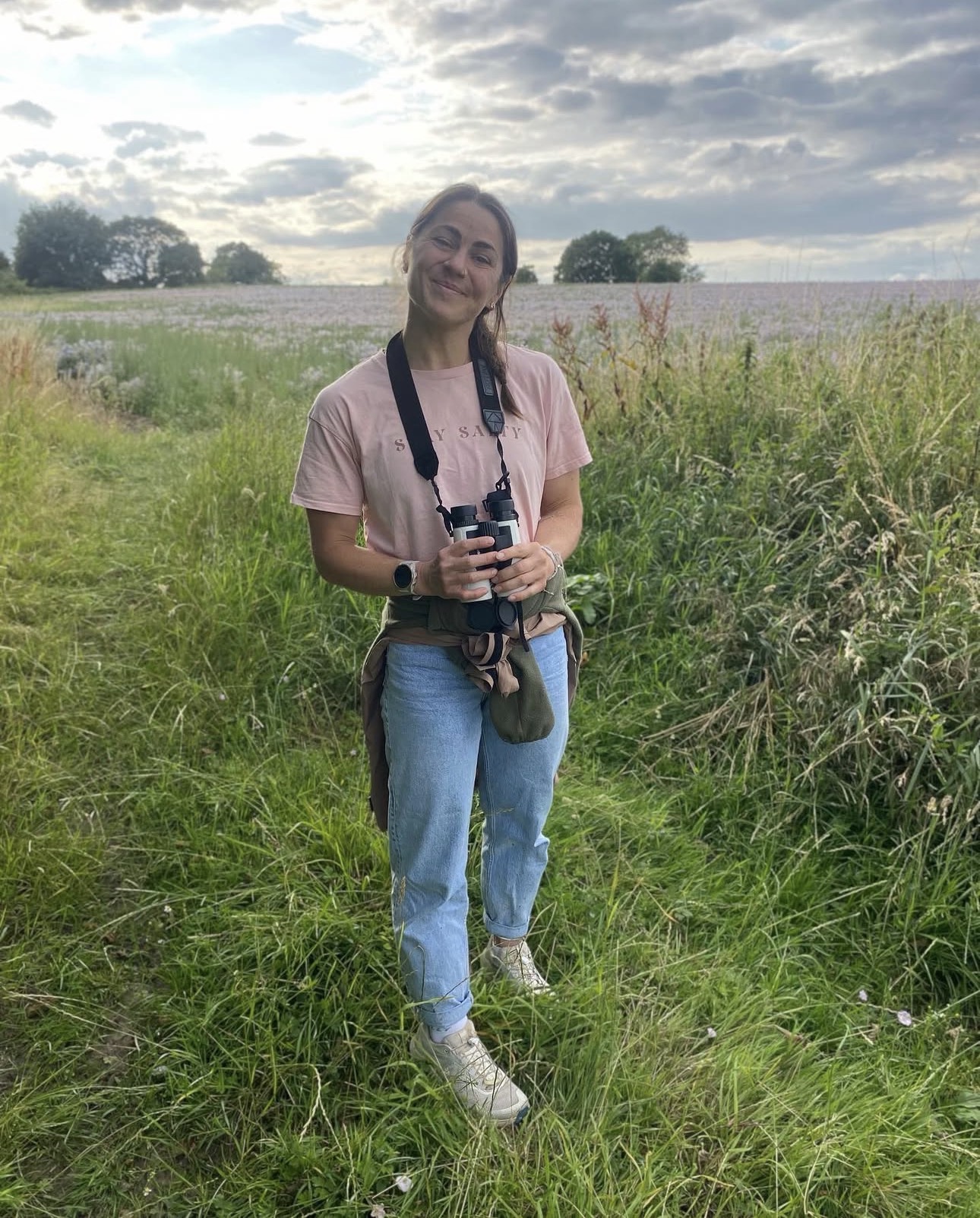Emelye standing in a wildflower field holding binoculars